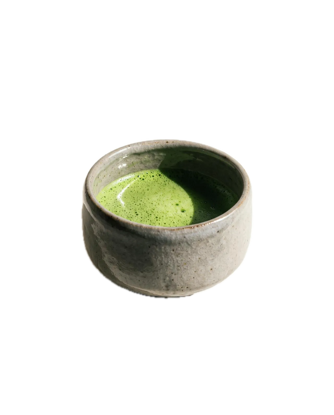 A pale speckled stoneware chawan holding whisked matcha, the foam pooled to one side.