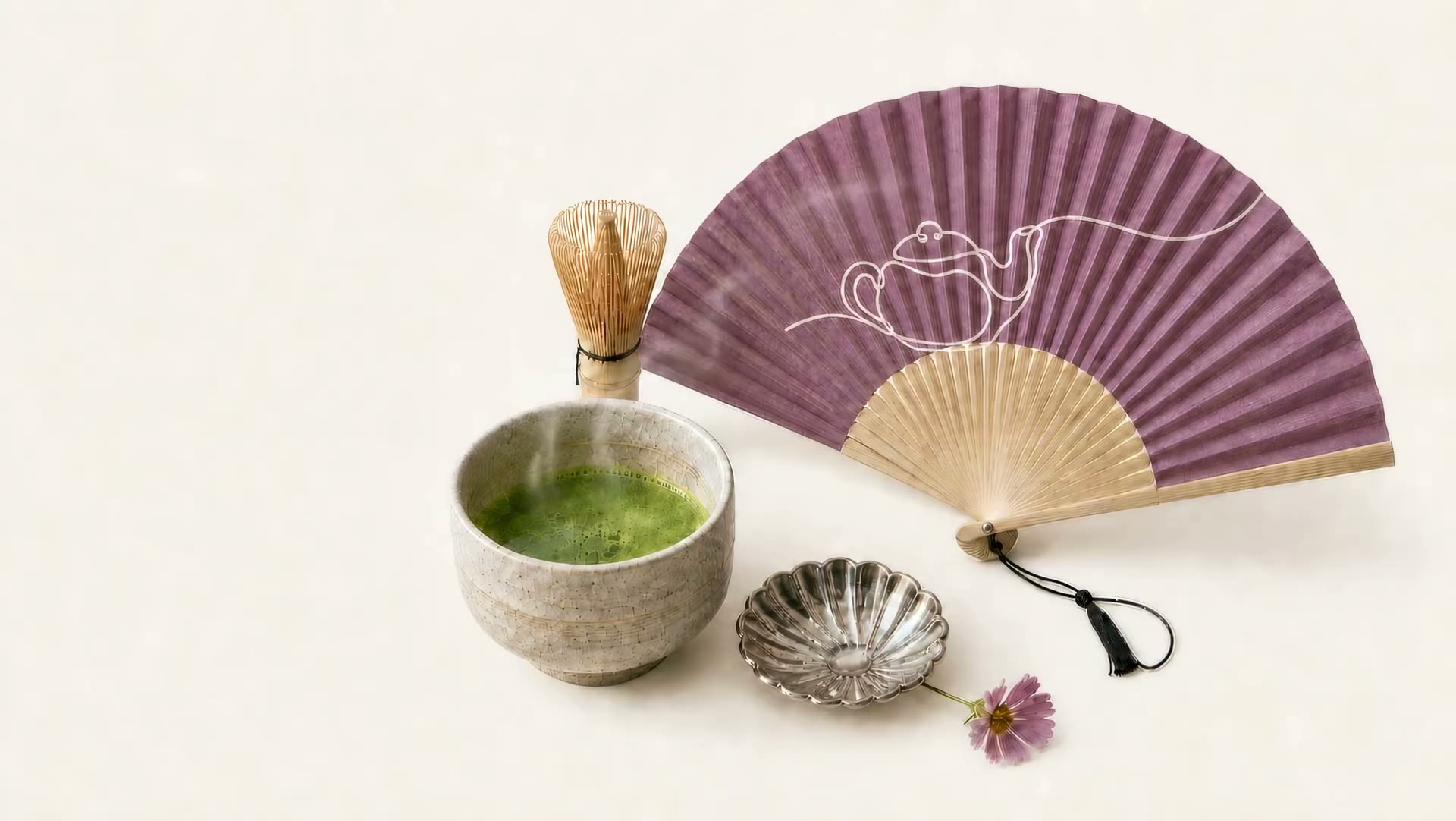 Editorial still life with matcha, a bamboo whisk, a mauve folding fan, a silver dish, and a mallow flower.